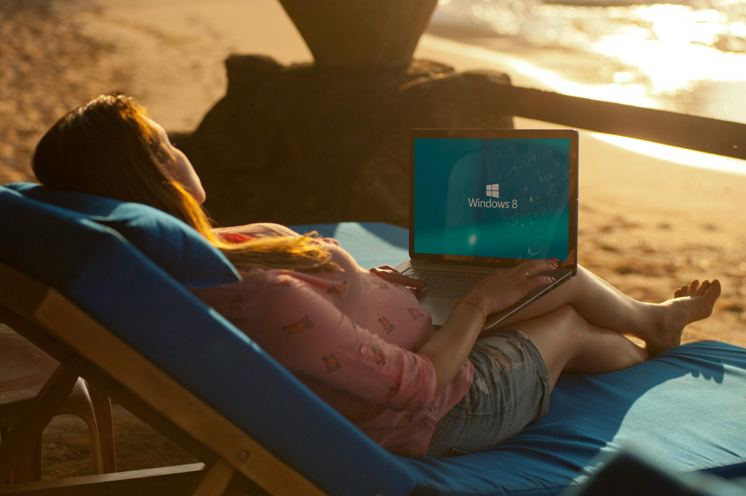 A woman lounging on a beach chair using a laptop, enjoying the sunny seashore.